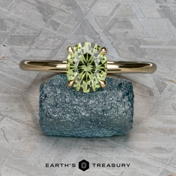 The "Begonia" ring in 14K yellow gold with 1.56-Carat Australian sapphire The "Begonia" ring in 14K yellow gold with a 1.56-carat Australian sapphire is displayed on a rough blue stone against a gray textured background, with the "Earth’s Treasury" logo at the bottom.