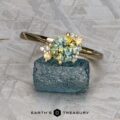 The "Nebula" ring in 14K yellow gold, featuring a 1.54-carat Montana sapphire and accent stones, is displayed on rough blue crystal with a geometric patterned background.