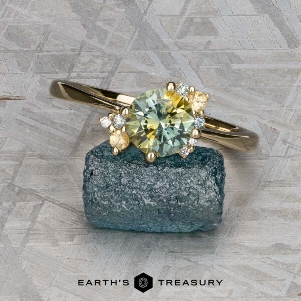 The "Nebula" ring in 14K yellow gold with 1.54-carat Montana sapphire The "Nebula" ring in 14K yellow gold, featuring a 1.54-carat Montana sapphire and accent stones, is displayed on rough blue crystal with a geometric patterned background.
