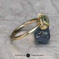 The "Nebula" ring in 14K yellow gold with a 1.54-carat Montana sapphire is shown atop a dark mineral rock, set against a textured gray background featuring the Earth's Treasury logo at the bottom.