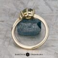 The "Nebula" ring in 14K yellow gold with a 1.54-carat Montana sapphire stands upright against a rough blue mineral on a textured gray surface. The text "EARTH'S TREASURY" appears at the bottom.