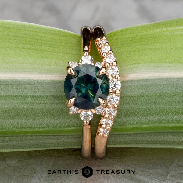 The "Lipara" ring in 20K pink gold with 1.70-carat Montana sapphire, alongside the "Hesperia" band in 20K pink gold The "Lipara" ring in 20K pink gold features a 1.70-carat Montana sapphire, shown with the "Hesperia" band, both on a green leaf background. The "Earth's Treasury" logo appears at the bottom.