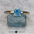 The "Clarice" ring in 14K yellow gold with a 0.97-carat Montana sapphire rests on a rough blue stone atop a textured gray surface, with "Earth's Treasury" written below.
