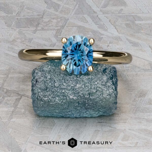 The "Clarice" ring in 14K yellow gold with 0.97-carat Montana sapphire The "Clarice" ring in 14K yellow gold with a 0.97-carat Montana sapphire rests on a rough blue stone atop a textured gray surface, with "Earth's Treasury" written below.
