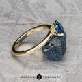 The "Clarice" ring in 14K yellow gold with a 0.97-carat Montana sapphire stands upright, balanced on a rough blue stone, with the "Earth's Treasury" logo at the bottom.