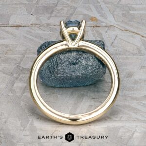 The "Clarice" ring in 14K yellow gold, featuring a 0.97-carat Montana sapphire in a prong setting, is displayed upright against a dark stone with the Earth's Treasury logo at the bottom.