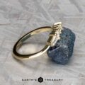 The "Mandevilla" band in 14K yellow gold, featuring a row of diamonds, rests against a rough, dark stone on a textured gray background. The "Earth’s Treasury" logo appears at the bottom of the image.