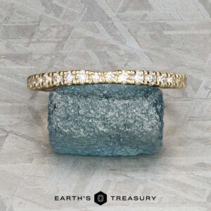 The Classic Pave Notched Band in 14K yellow gold is displayed on a rough blue gemstone against a textured gray background, with the logo "EARTH'S TREASURY" visible at the bottom.