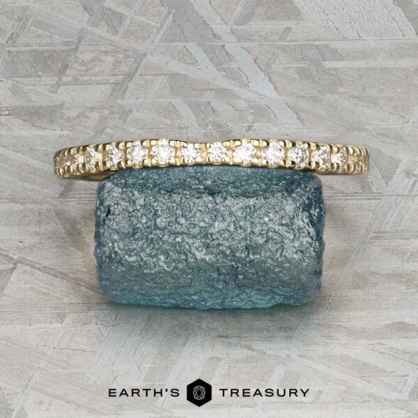 The Classic Pave Notched Band in 14K yellow gold is displayed on a rough blue gemstone against a textured gray background, with the logo "EARTH'S TREASURY" visible at the bottom.