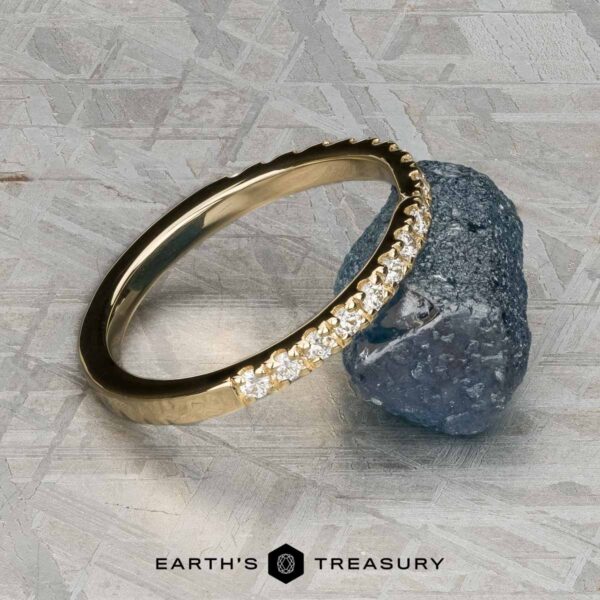 The Classic Pave Notched Band in 14K yellow gold The Classic Pave Notched Band in 14K yellow gold, featuring a row of small diamonds, rests on a rough blue stone against a textured gray background. "EARTH'S TREASURY" is shown at the bottom.