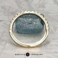 The Classic Pave Notched Band in 14K yellow gold is displayed upright before a rough blue stone on a gray patterned surface, with "EARTH'S TREASURY" at the bottom.