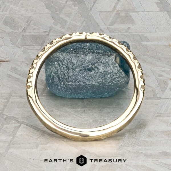 The Classic Pave Notched Band in 14K yellow gold The Classic Pave Notched Band in 14K yellow gold is displayed upright before a rough blue stone on a gray patterned surface, with "EARTH'S TREASURY" at the bottom.