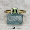 The "Larisa" ring in 18K yellow gold featuring a 1.04-carat Australian sapphire is displayed on a rough blue stone, with the "Earth’s Treasury" logo and name at the bottom.
