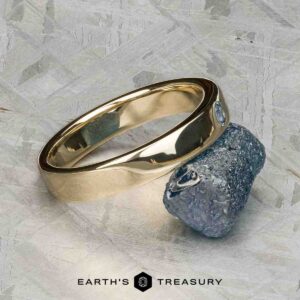 The "Denali" ring in 14K yellow gold is shown beside a rough, uncut stone on a light textured surface, with the Earth's Treasury logo displayed below.