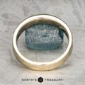 The "Denali" ring in 14K yellow gold stands upright before a rough blue gemstone on a textured gray surface. The logo and "EARTH'S TREASURY" text appear at the bottom of the image.