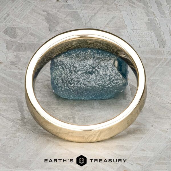 The "Denali" ring in 14K yellow gold The "Denali" ring in 14K yellow gold stands upright before a rough blue gemstone on a textured gray surface. The logo and "EARTH'S TREASURY" text appear at the bottom of the image.
