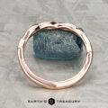 The Minimal “Lonicera” band in 14K rose gold is elegantly balanced on a rough blue gemstone, with “EARTH’S TREASURY” displayed beneath on a textured gray background.