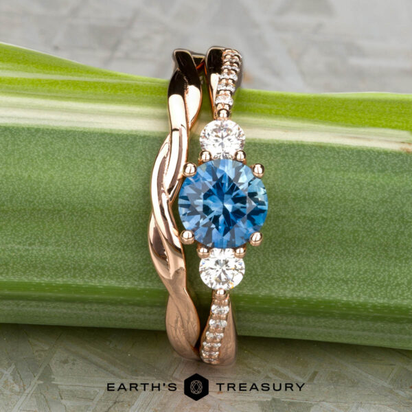 The "Lonicera" ring in 14K rose gold with 0.93-carat Montana sapphire, alongside the minimal "Lonicera" band in 14K rose gold The "Lonicera" ring in 14K rose gold features a 0.93-carat Montana sapphire center, two side diamonds, and small band diamonds, shown with the minimal "Lonicera" band in 14K rose gold against a green stem.