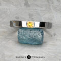The "Kilimanjaro" ring in 14K white gold, featuring a rectangular yellow gemstone, is displayed balanced on a rough blue stone with the Earth's Treasury logo beneath.