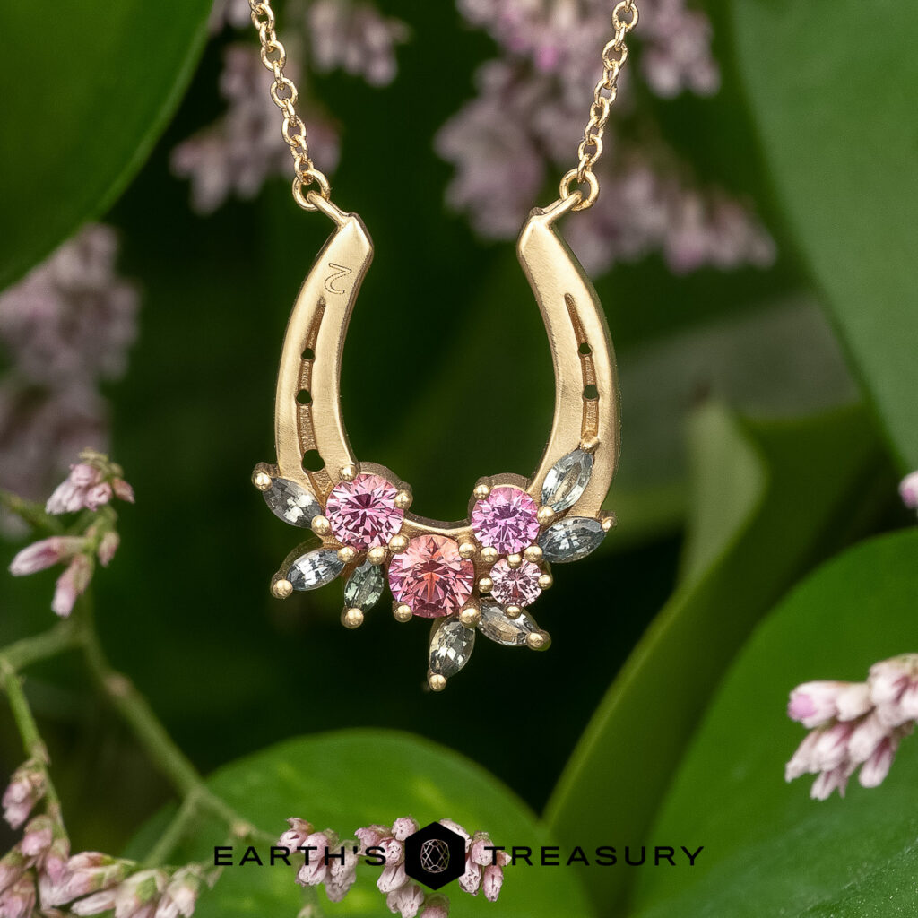 The "Stacked from 14 images. Method=B (R=14,S=2)" necklace, gold and horseshoe-shaped with pink and clear gemstones, is displayed among green leaves and pink flowers.