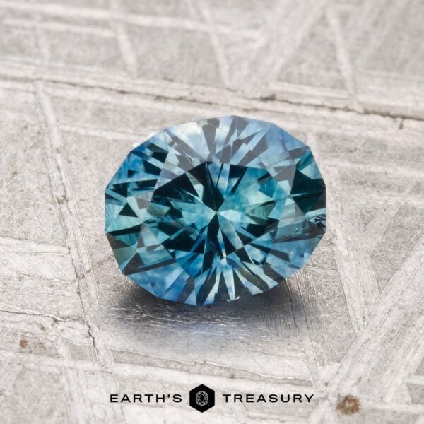 1.31-Carat Montana Sapphire (Heated) A 1.31-carat heated Montana sapphire with a radiant cut rests on a textured gray surface, with the Earth's Treasury logo displayed at the bottom.