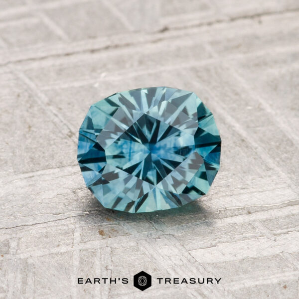 1.03-Carat Montana Sapphire (Heated) A 1.03-carat heated Montana sapphire with a blue square cushion cut rests on a textured gray surface, with "EARTH'S TREASURY" text below.