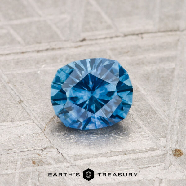 0.88-Carat Montana Sapphire (Heated) A faceted 0.88-carat heated Montana sapphire rests on a light-textured surface, with "EARTH'S TREASURY" and logo displayed at the bottom.