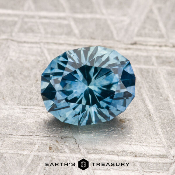 1.48-Carat Montana Sapphire (Heated) A 1.48-carat heated Montana sapphire is displayed on a textured metallic surface, with the "Earth's Treasury" logo and text at the bottom.