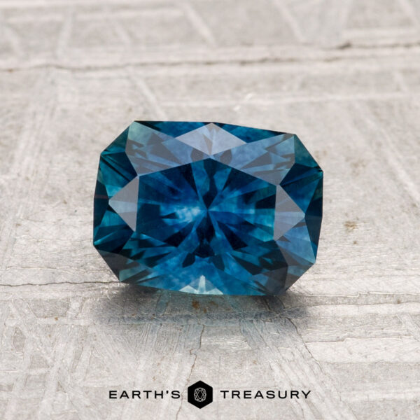 1.67-Carat Montana Sapphire (Heated) A 1.67-carat heated Montana sapphire with a rectangular cushion cut rests on a textured gray surface displaying the "Earth's Treasury" logo.