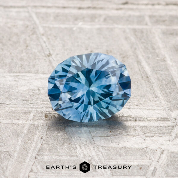 1.01-Carat Montana Sapphire (Heated) A 1.01-carat heated Montana sapphire is showcased on a textured, light-colored surface with “EARTH’S TREASURY” displayed at the bottom.