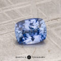 A 1.24-carat cushion-cut Ceylon sapphire rests on a textured gray surface with "Earth's Treasury" displayed at the bottom.