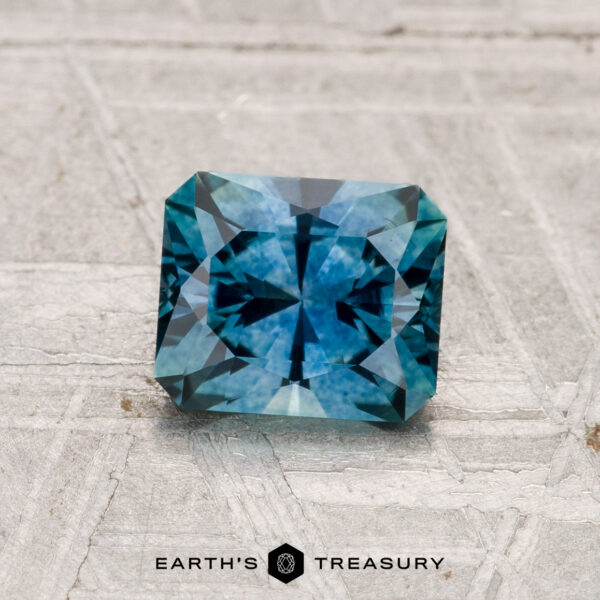 1.16-Carat Montana Sapphire (Heated) A 1.16-carat rectangular step-cut heated Montana sapphire is displayed on a textured gray surface with "EARTH'S TREASURY" text at the bottom.