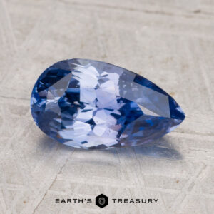 A faceted pear-shaped 2.27-Carat Ceylon Sapphire in violet-blue rests on a textured surface, with "EARTH'S TREASURY" displayed at the bottom.