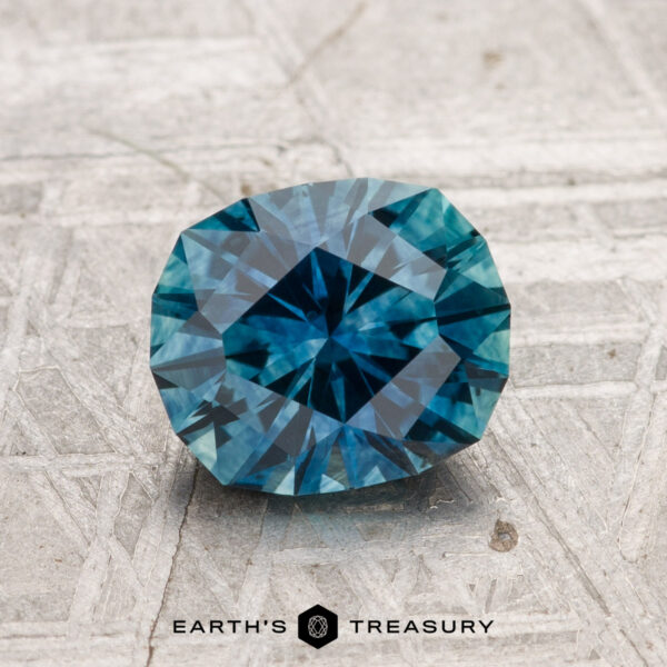 1.61-Carat Montana Sapphire (Heated) A 1.61-carat heated Montana sapphire with geometric facets is displayed on a textured gray surface. "EARTH'S TREASURY" appears at the bottom.