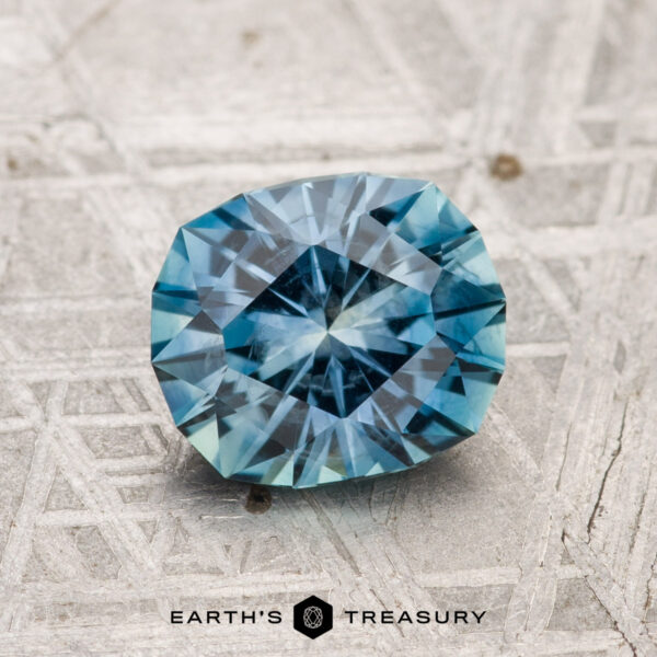 1.57-Carat Montana Sapphire (Heated) A 1.57-carat heated Montana sapphire is shown on a patterned metallic surface with "Earth's Treasury" visible at the bottom.