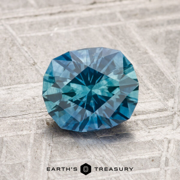 1.52-Carat Montana Sapphire (Heated) A 1.52-carat heated Montana sapphire with a blue octagonal facet rests on a textured gray surface; the "Earth's Treasury" logo appears at the bottom.