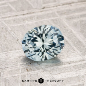 A 1.10-carat heated Montana sapphire, faceted in an oval cut, is shown on a textured light surface with the Earth's Treasury logo below.