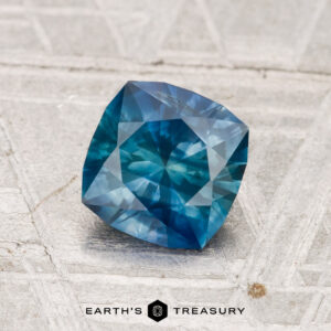 A 1.24-carat heated Montana sapphire, square-cut with a faceted surface, is displayed on a textured light background with "EARTH'S TREASURY" shown at the bottom.