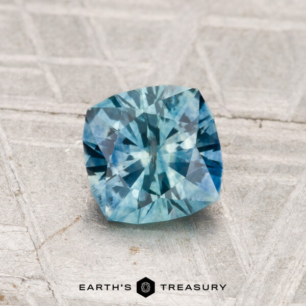 1.08-Carat Montana Sapphire (Heated) A cushion-cut 1.08-carat heated Montana sapphire displayed on a textured light gray surface with "EARTH'S TREASURY" below.