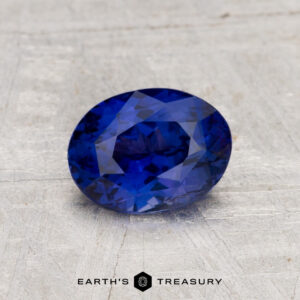 1.44-Carat Ceylon Sapphire, oval-cut and blue, displayed on a light gray textured surface with the "Earth's Treasury" logo at the bottom.
