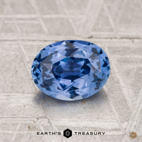 1.62-Carat Ceylon Sapphire A 1.62-carat Ceylon Sapphire, faceted and oval-shaped, rests on a patterned metallic surface with "EARTH'S TREASURY" displayed below.