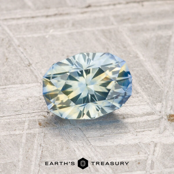 1.21-Carat Montana Sapphire (Heated) A 1.21-carat heated Montana sapphire with blue and yellow hues is displayed on a textured gray surface with the text "EARTH'S TREASURY" below.