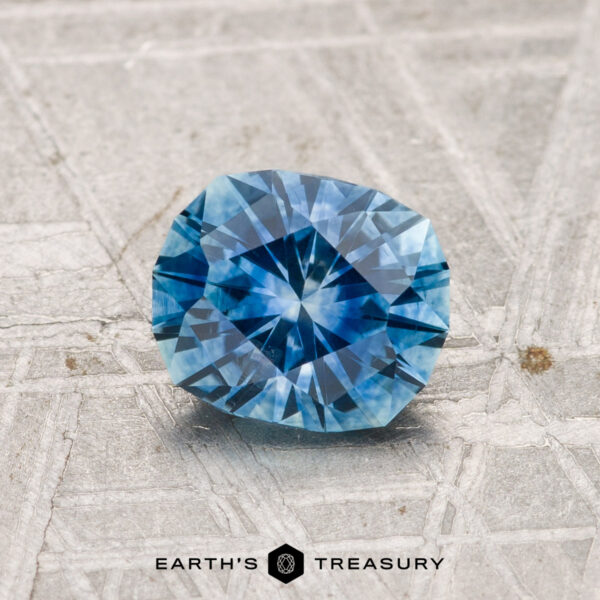 1.19-Carat Montana Sapphire (Heated) A 1.19-carat heated Montana sapphire rests on a textured grey surface, with "EARTH'S TREASURY" displayed at the bottom.