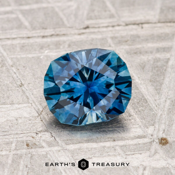 1.19-Carat Montana Sapphire (Heated) A 1.19-carat heated Montana sapphire with a blue hue rests on a textured gray surface, featuring the text "EARTH'S TREASURY" below.