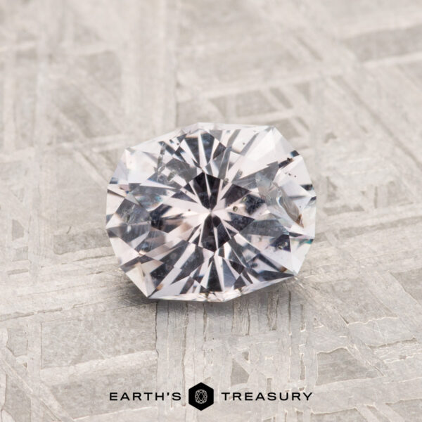 1.11-Carat Montana Sapphire A 1.11-carat Montana Sapphire, round and faceted, rests on a textured metallic surface with "Earth's Treasury" displayed below.