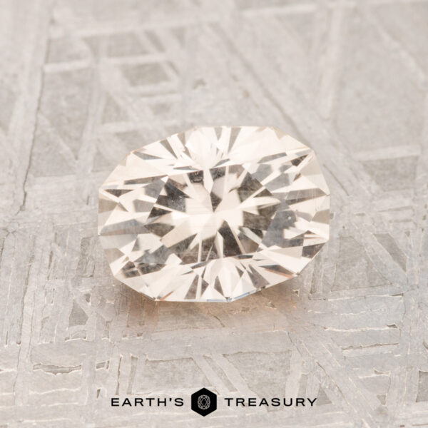 1.37-Carat Montana Sapphire A faceted, clear 1.37-carat Montana sapphire is displayed on a textured metallic surface featuring "EARTH'S TREASURY" and a logo at the bottom center.