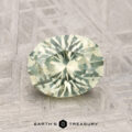 A 1.79-carat Montana Sapphire, faceted in a pale green oval, is displayed on a textured metallic surface with "EARTH'S TREASURY" shown below.