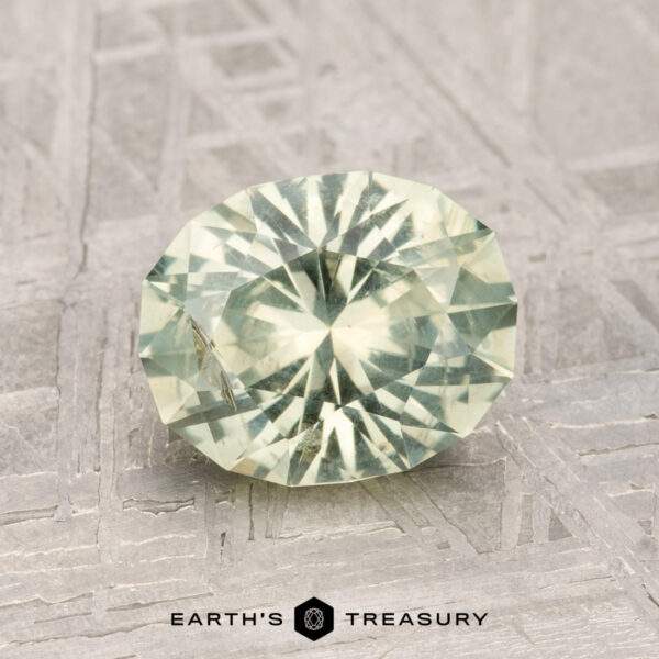 1.79-Carat Montana Sapphire A 1.79-carat Montana Sapphire, faceted in a pale green oval, is displayed on a textured metallic surface with "EARTH'S TREASURY" shown below.