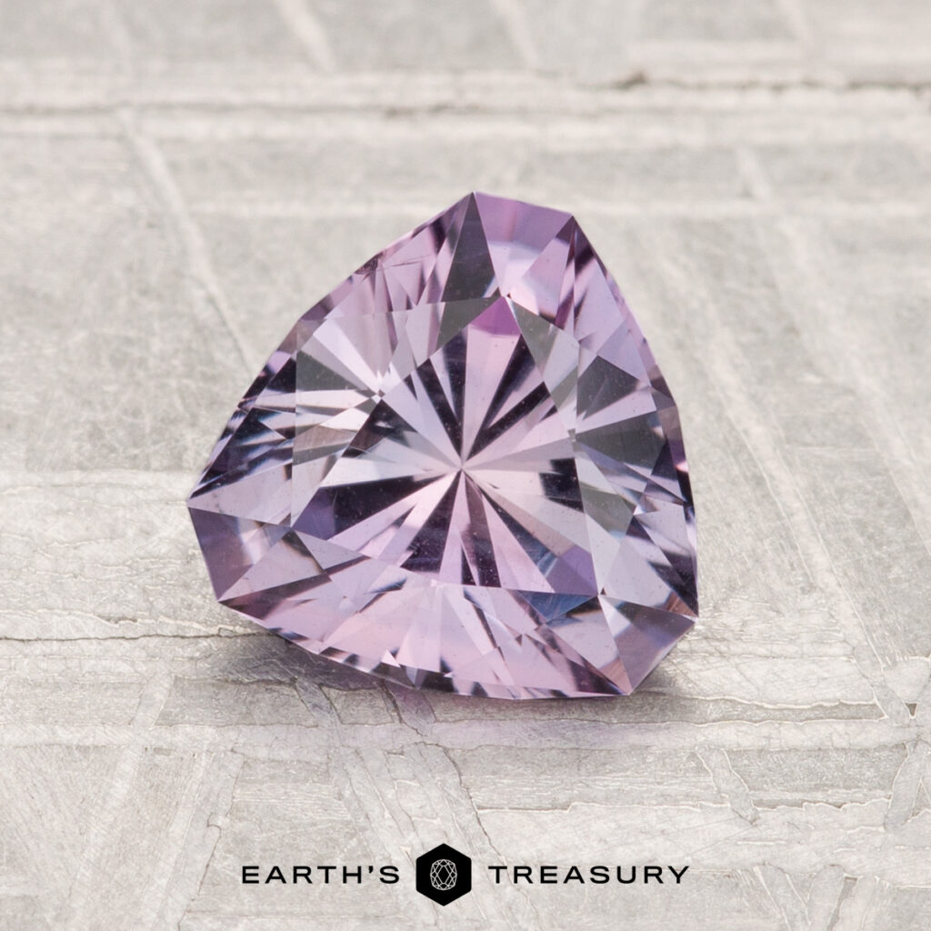 A 1.42-carat trilliant-cut light purple Montana Sapphire displayed on a textured surface with the Earth's Treasury logo at the bottom.