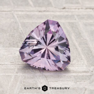 A 1.42-carat trilliant-cut light purple Montana Sapphire displayed on a textured surface with the Earth's Treasury logo at the bottom.